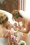 Candid wedding photograph of a bride putting lipstick on her daughter and flower girl