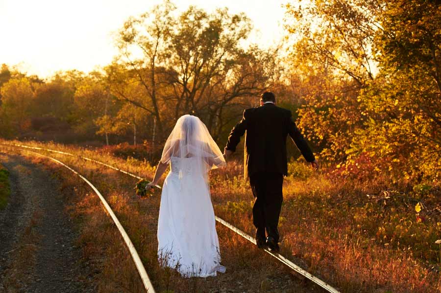 Wedding photograph of a bride and groom walking along train tracks into the sunset with fall colours